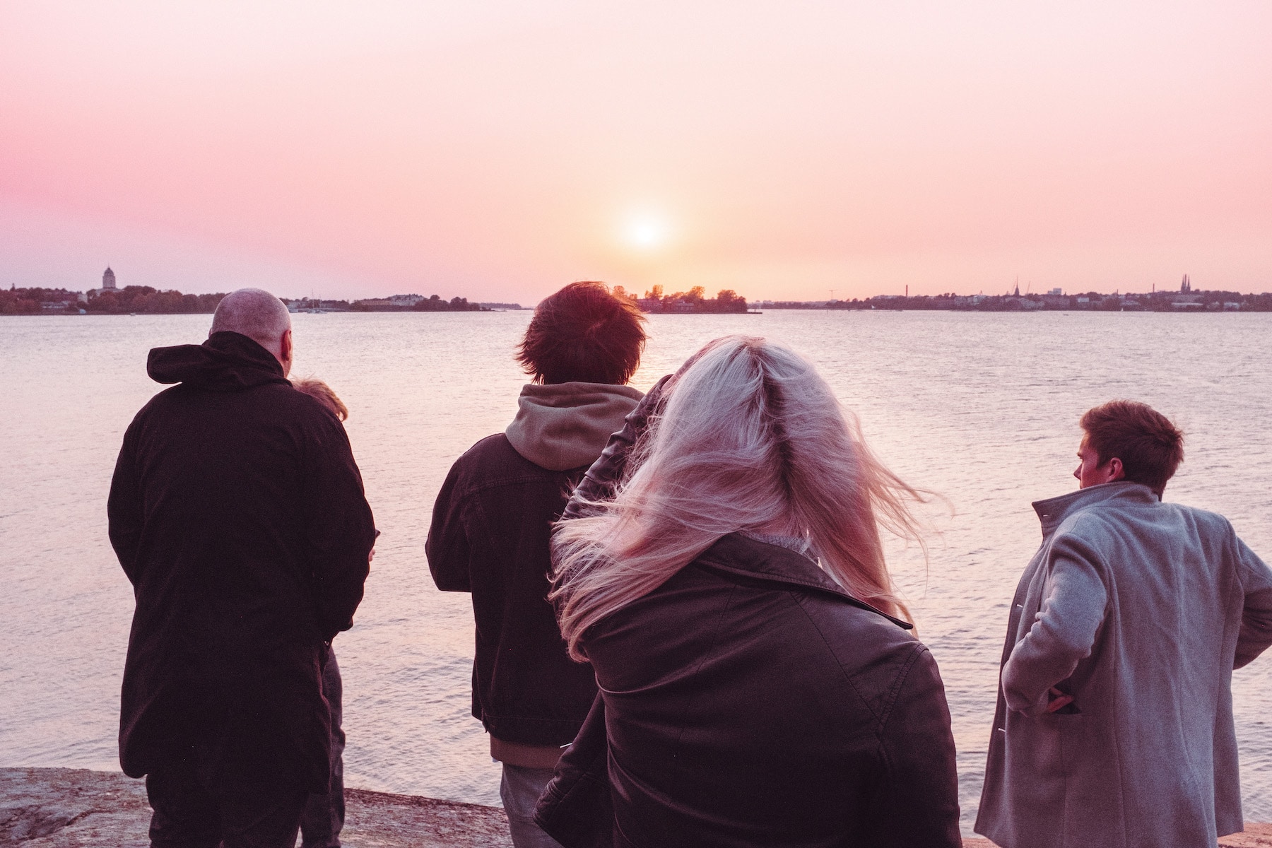 Ihmiset seisovat meren äärellä auringonlaskussa ja katsovat merelle päin.