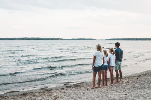 Perhe, jossa on äiti, isä ja kaksi tytärtä katselevat horisonttiin tuulisella rannalla.